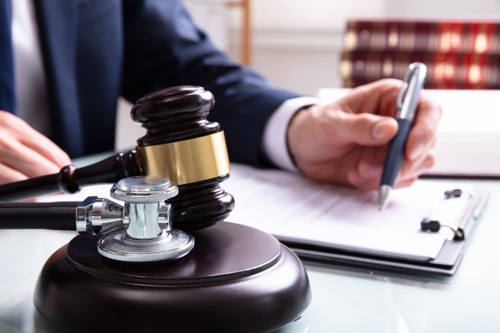 Medical malpractice lawyer writing on a legal Document with mallet and stethoscope over sound block in Court.